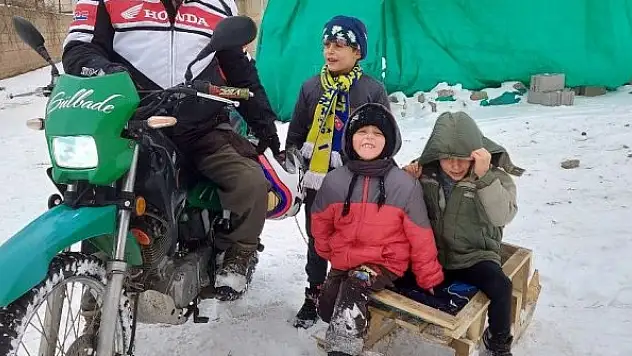 Motosiklete bağladığı kızaklarla çocukları karda eğlendirdi
